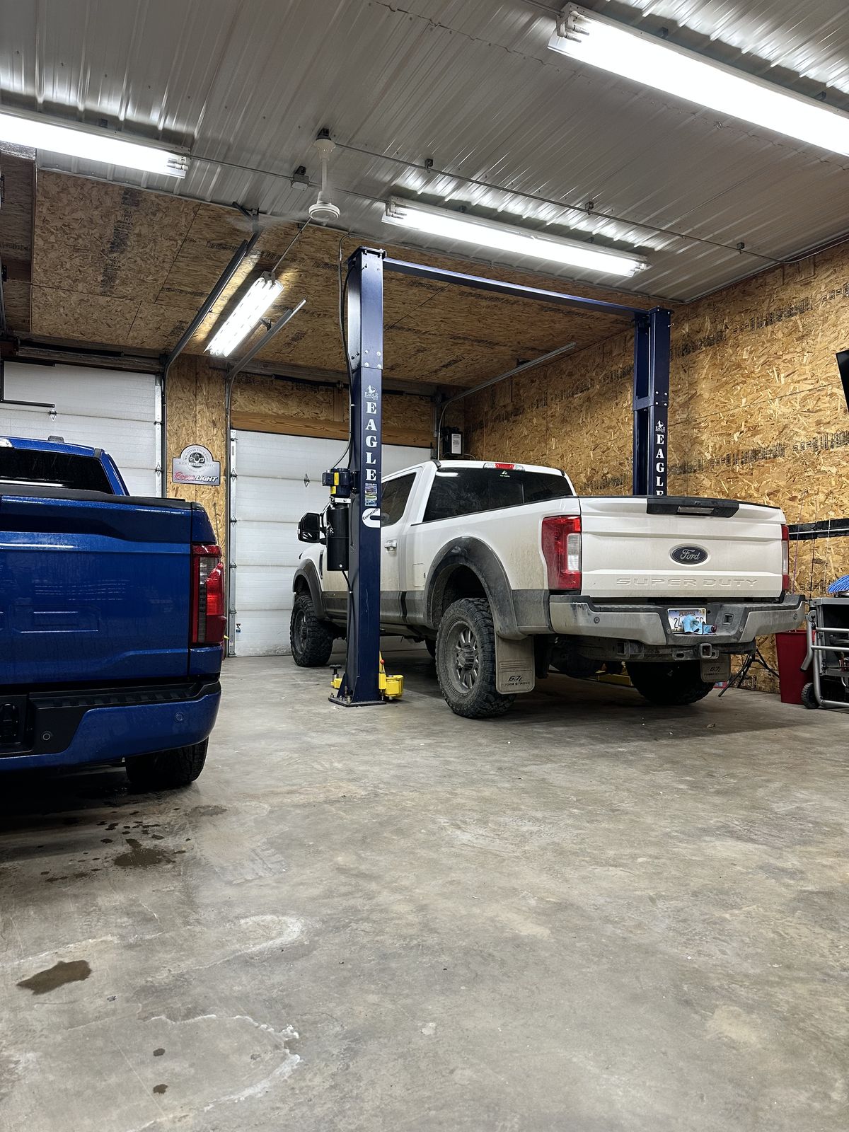 White Ford Super Duty on the Eagle lift in the Chinook shop, blue F-150 in the bay